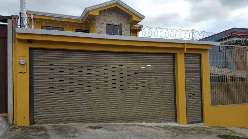 cortina metalica color café en casa color amarillo con una puerta a la par